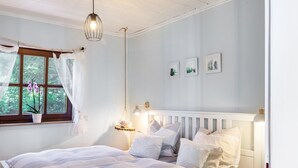 Quarto com cama, janela com cortinas, luminária pendente e quadros na parede.
