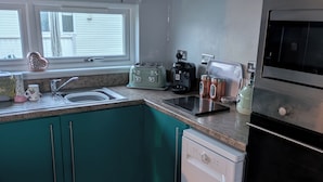 A kitchen with teal cabinets, a dishwasher, a stove, a toaster, a coffee maker, and a sink. - Caravan - Sleeps 6 - Short Walk to Rhyl Beach (Rhyl)