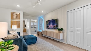 Ein modernes Wohnzimmer mit einem blauen Sofa, einem flachbildfernseher, der an einer weißen Wand montiert ist, und einer Holzkommode darunter.