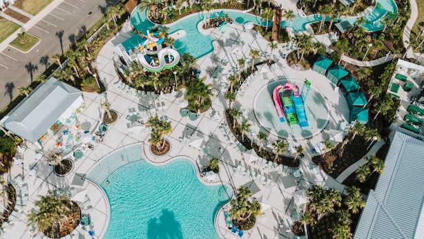 Luftaufnahme eines Resorts mit großem zentralem Pool, mehreren Wasserrutschen und Liegestühlen.