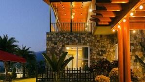 Une maison à deux étages avec une façade en pierre, un balcon doté de balustrades en bois et une entrée bien éclairée.