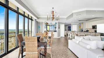 A spacious living area with a dining table, white sofas, and a large window offering a view.