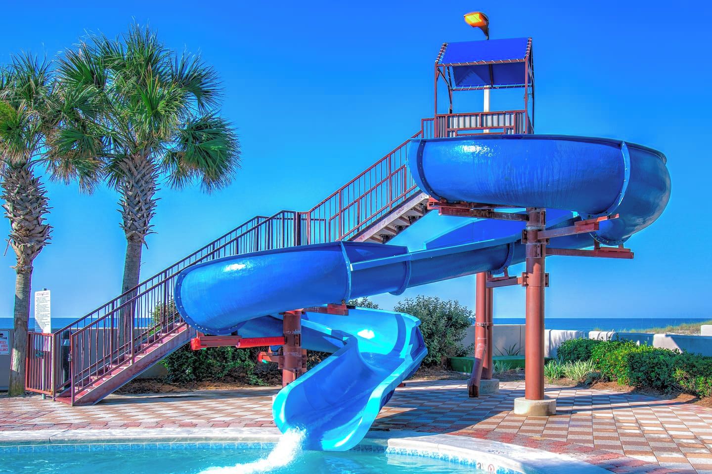 A water park with a multi-level water slide structure, a pool, and palm trees.