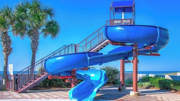 A water park with a multi-level water slide structure, a pool, and palm trees.