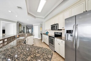 Cocina moderna con encimeras de granito, electrodomésticos de acero inoxidable y armarios blancos.