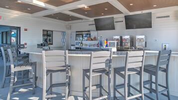 A bar area with a counter and bar stools, a television mounted on the wall, and a refrigerator stocked with beverages.