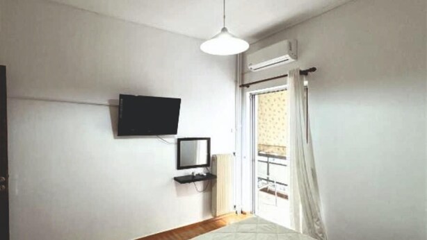 A bedroom with a bed, a television mounted on the wall, and a window with curtains. - An Athenian gem by the Acropolis (Athens)