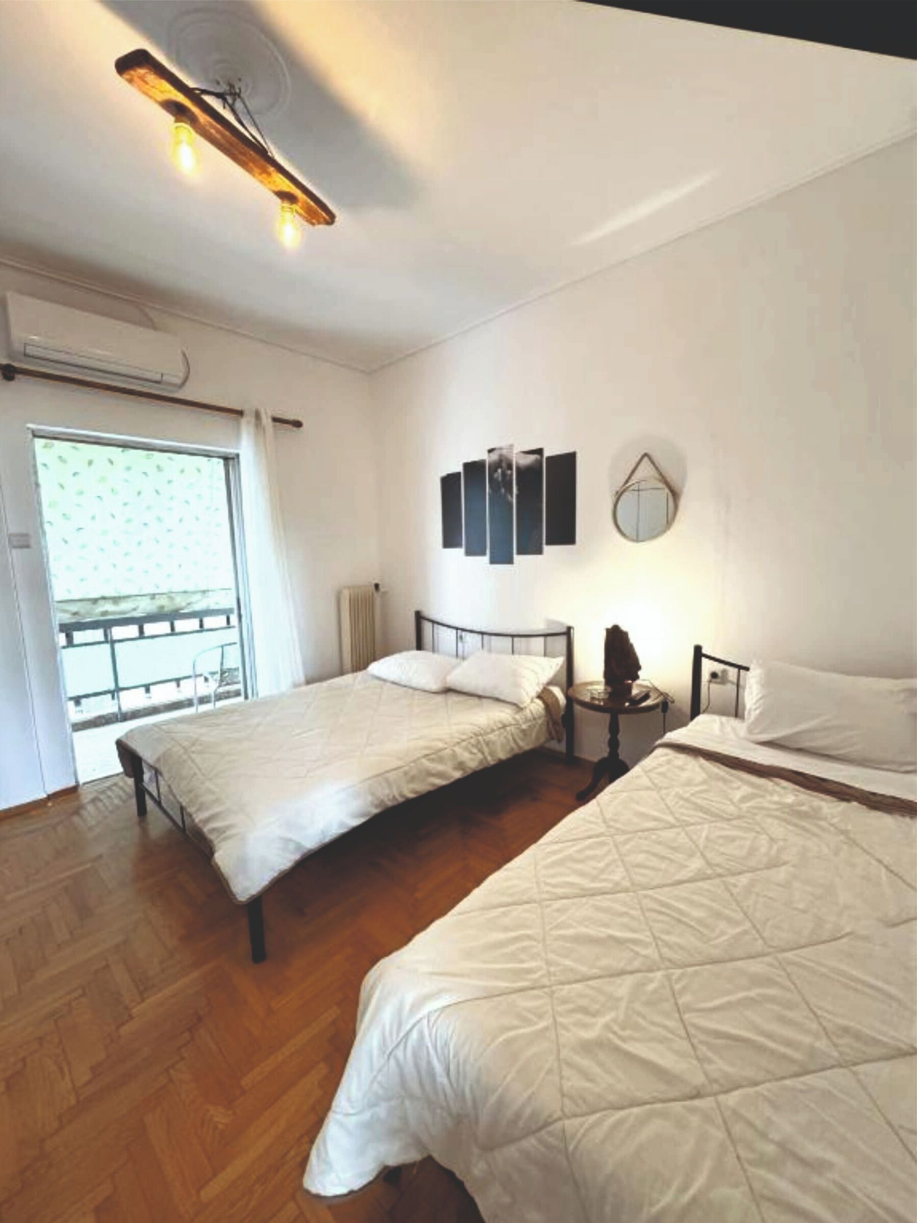 A bedroom with two beds, a ceiling light fixture, a window with curtains, and a wall-mounted mirror.