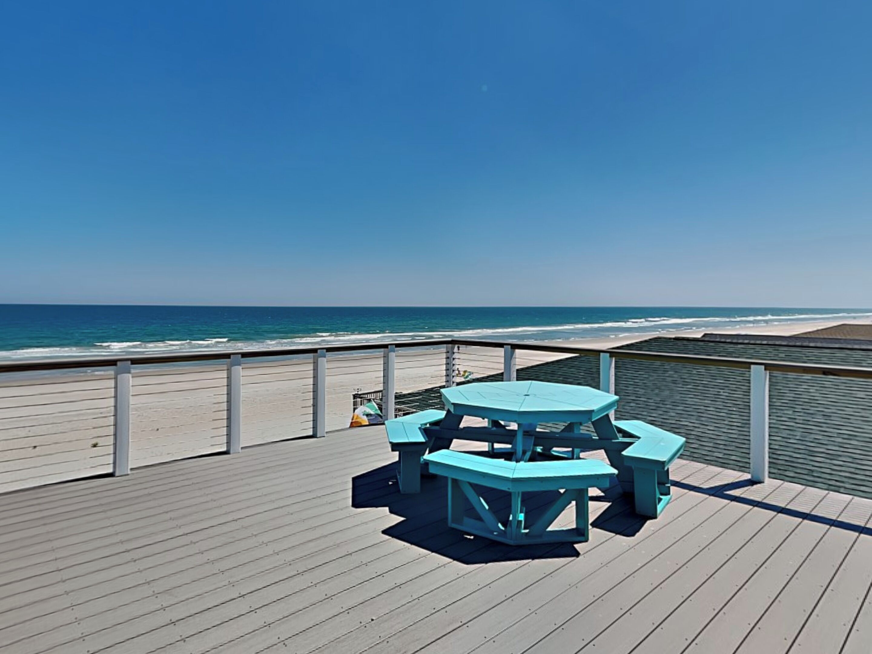 A wooden deck with a picnic table and benches overlooking the beach.
