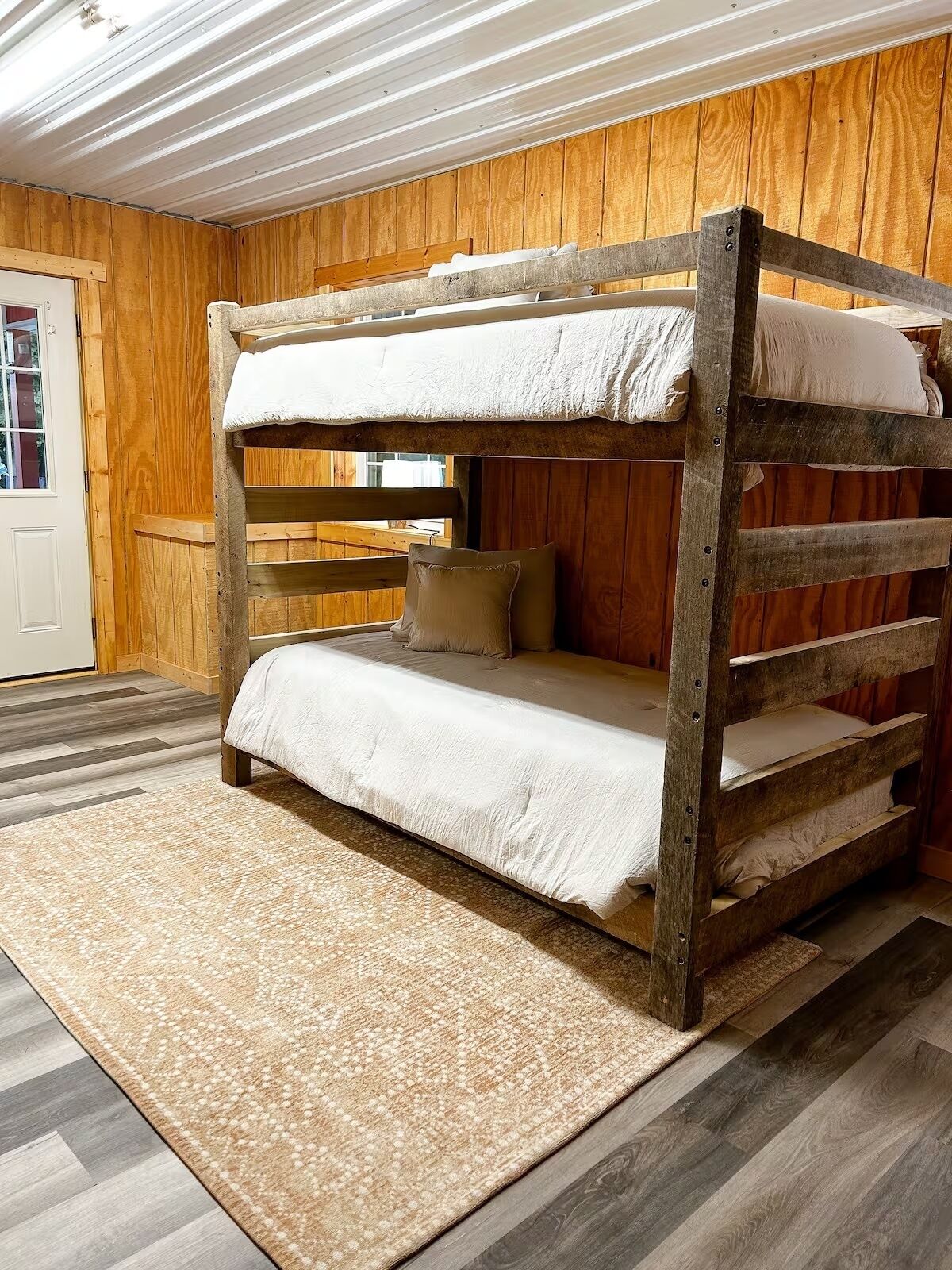 Een stapelbed met een houten hoofdbord, een tapijt met een patroon en een houten vloer.