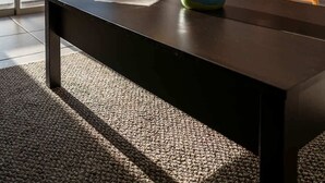 Ein moderner Essbereich mit einem dunklen Holztisch, einer bunten Vase mit gelben Blumen und Blick durch große Fenster.