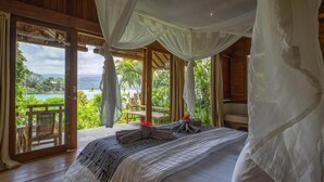 A bedroom with a canopy bed, a view of a tropical landscape, and a wooden deck outside. - D'Lagoon Dive Resort (Pulau Lembeh)