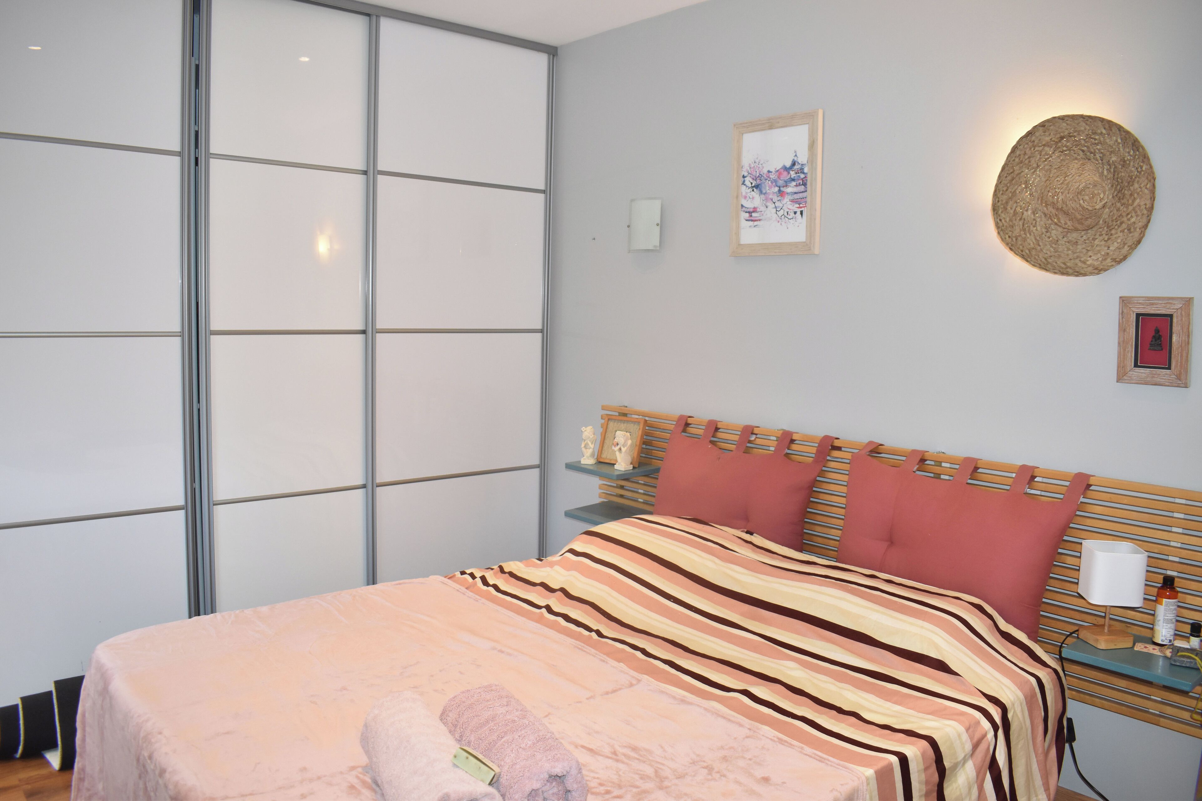 A hotel room with a bed, a nightstand, a wall-mounted lamp, and a framed picture.