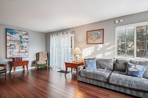 A living room with a wooden floor, a sofa, a chair, a lamp, and a painting on the wall.