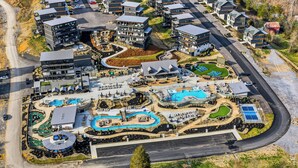 Ett flygbildsfoto av ett semesterområde med flera byggnader, ett slingrande poolområde och en stor huvudbyggnad med ett välvt tak.