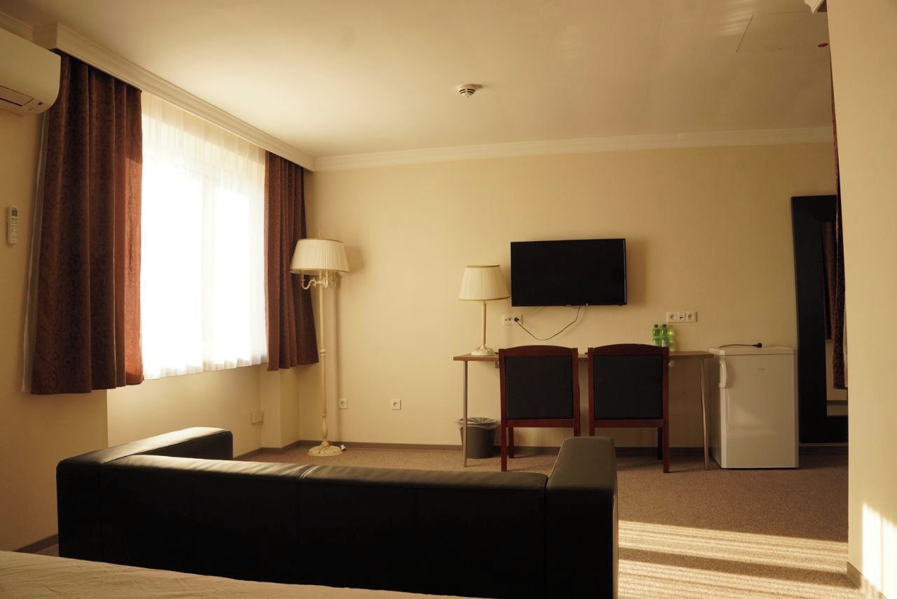 Une chambre d’hôtel équipée d’un lit, d’un bureau, d’une télévision, d’un réfrigérateur et d’une fenêtre avec des rideaux.