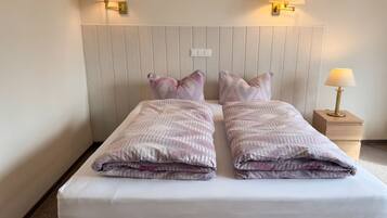 Een tweepersoonsbed met een witte matras en twee kussens, een houten hoofdbord en twee wandlampen.