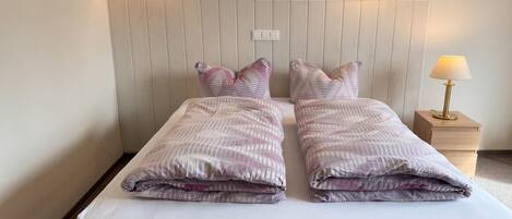 A double bed with a white mattress and two pillows, a wooden headboard, and two wall-mounted lamps.