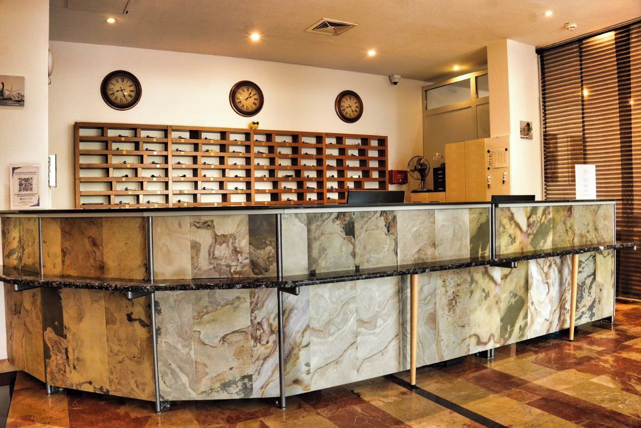 Una recepción con encimera de mármol, varios relojes en la pared y una botellera detrás.