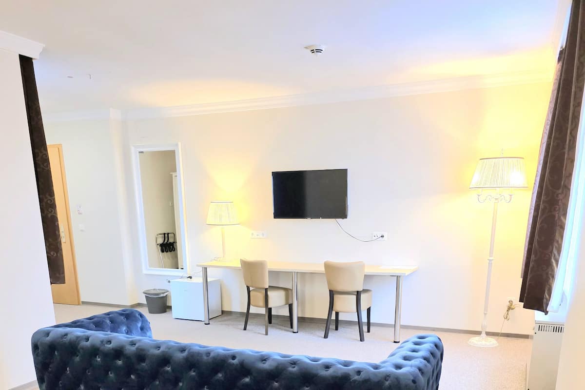 A hotel room with a large bed, a smaller bed, a desk with two chairs, a flat-screen TV, a lamp, and a ceiling-mounted smoke detector.