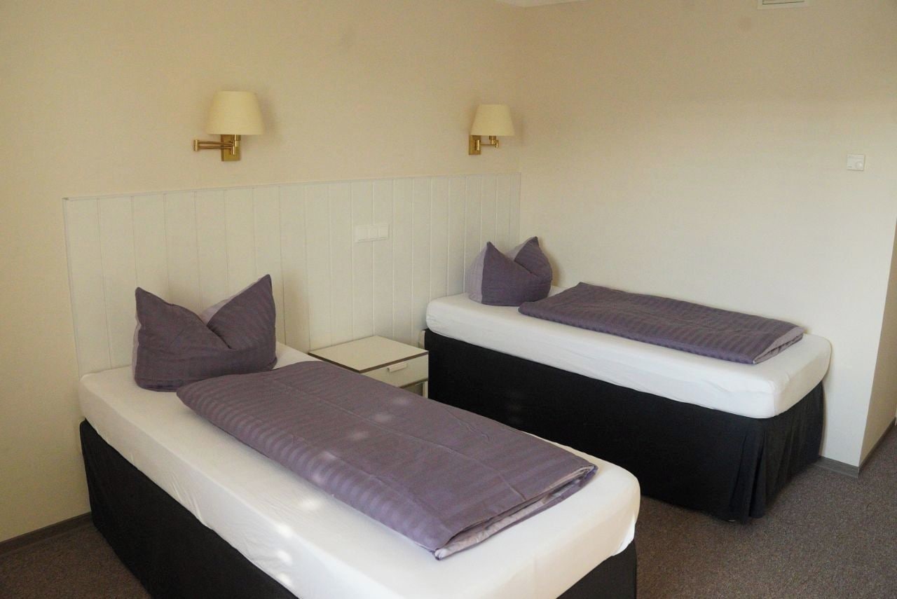 Une chambre comprenant deux lits simples avec des têtes de lit, des tables de chevet et des lampes fixées au mur.