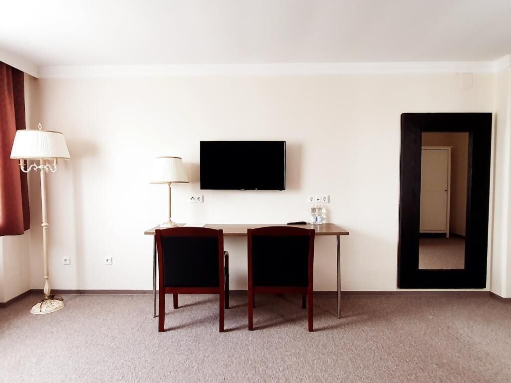 Habitación de hotel con escritorio, dos sillas, televisor de pantalla plana, lámpara y puerta que da a otra habitación.