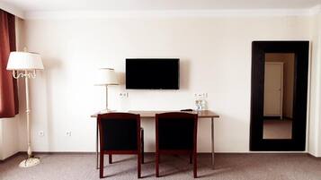 Habitación de hotel con escritorio, dos sillas, televisor de pantalla plana, lámpara y puerta que da a otra habitación.