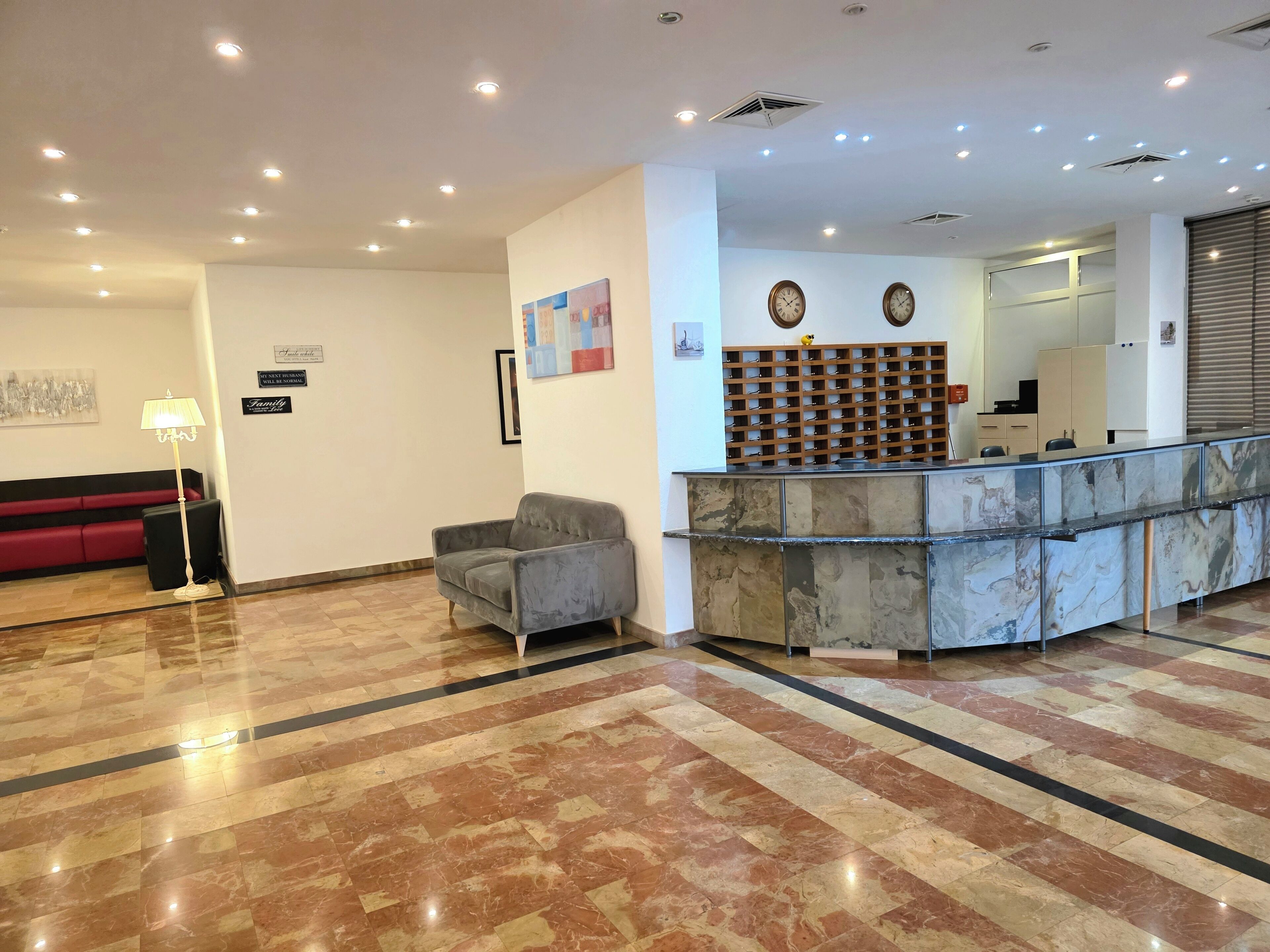 A reception area with a marble floor, a grey armchair, a red couch, and a reception desk with a marble top.