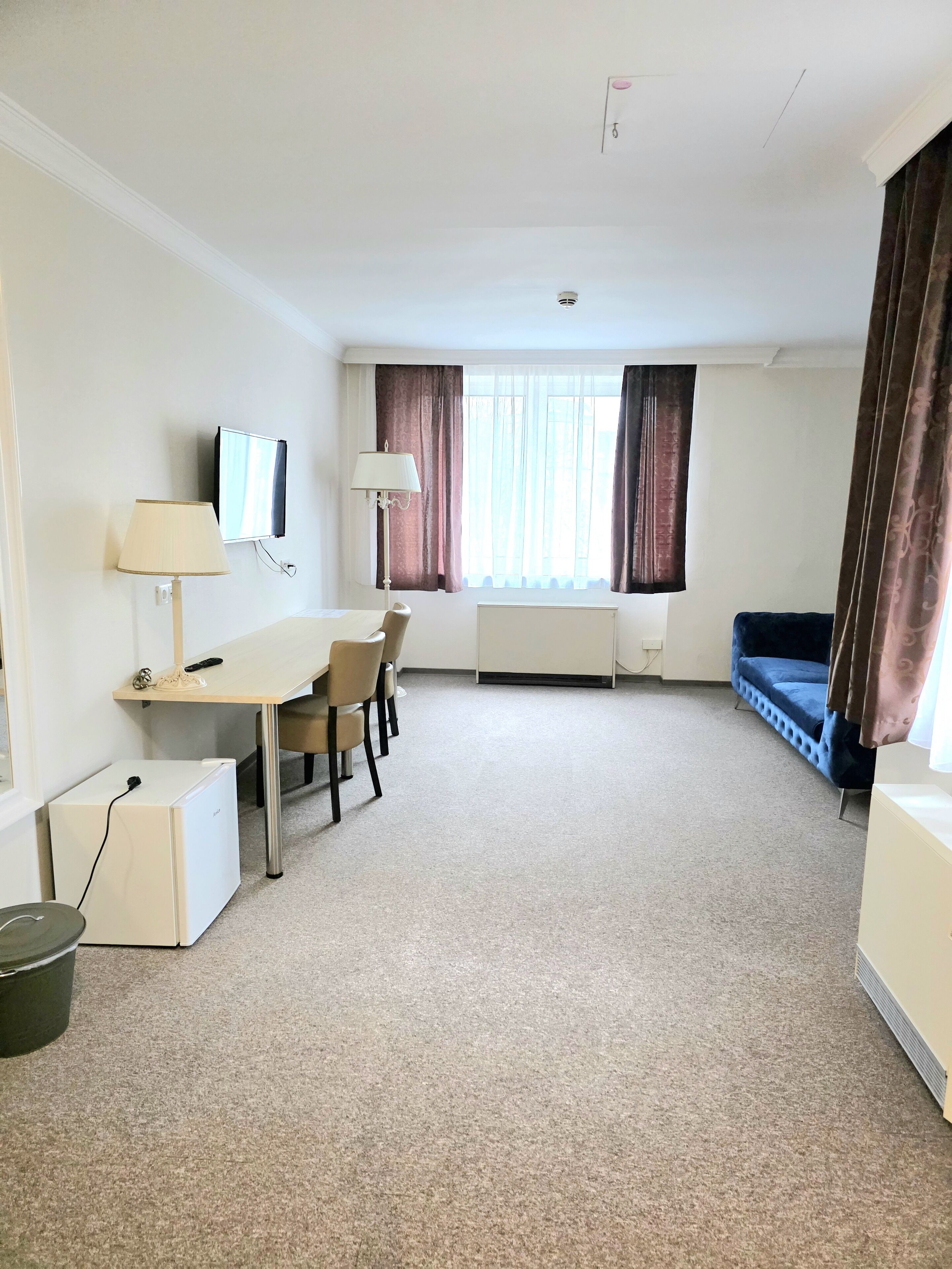 Una habitación de hotel con cama, escritorio con silla, televisión y ventana con cortinas.