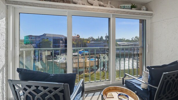 Een balkon met uitzicht op een zwembad en gebouwen, voorzien van stoelen en een tafel.