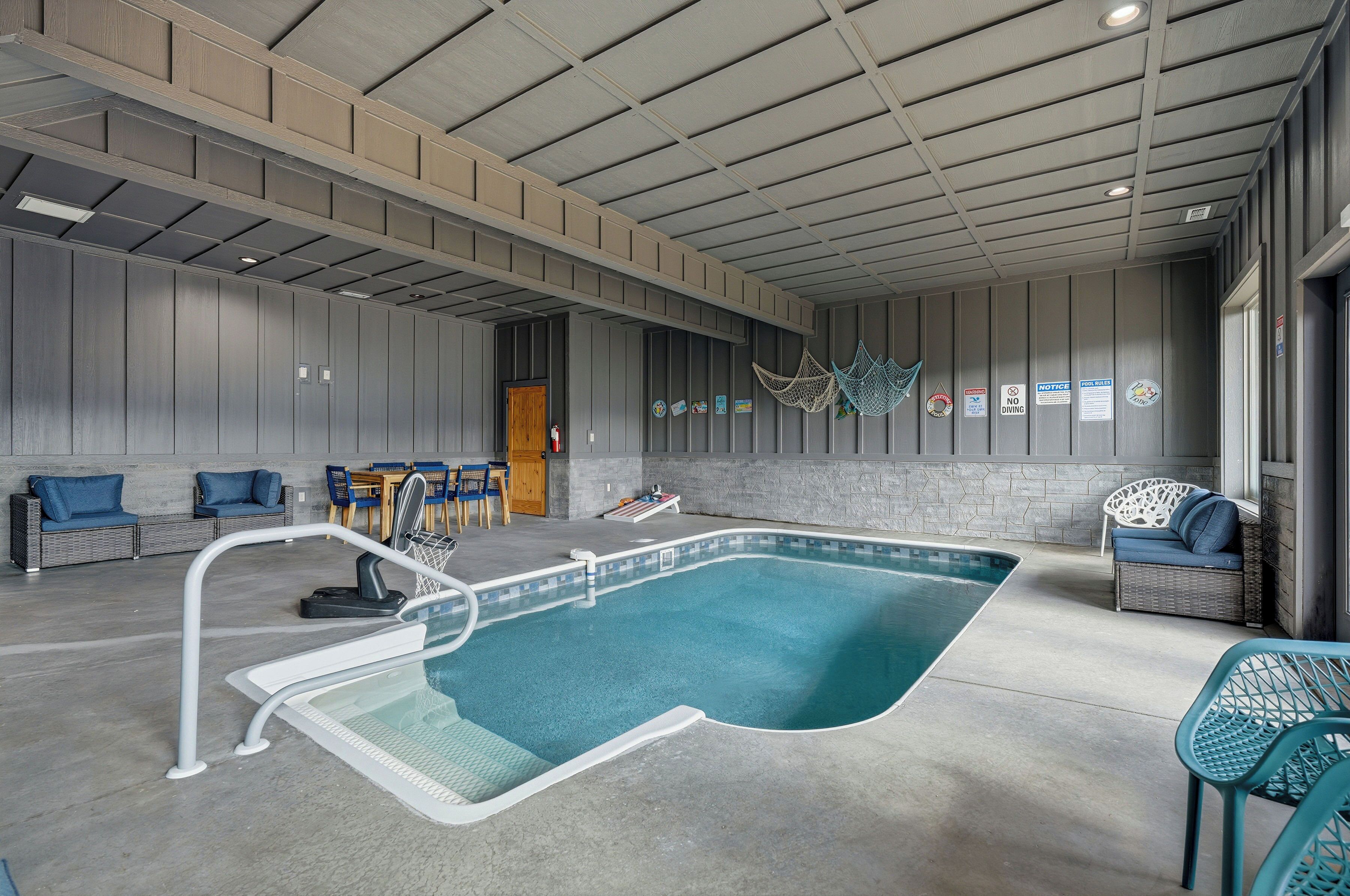 An indoor swimming pool with a concrete floor, surrounded by wicker furniture and a stone wall.