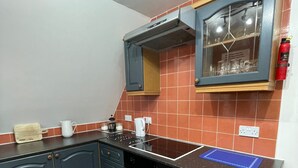 Keittiössä on tummansiniset kaapit, musta työtaso ja punaisilla laatoilla päällystetty seinäosa.
