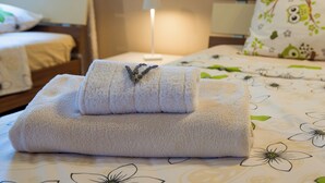 Een opgemaakt bed met een gevouwen handdoek en een bedlampje.