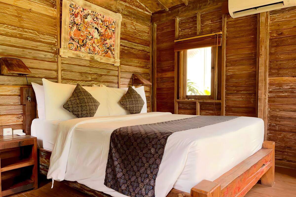 Una habitación de madera con una cama, una mesita de noche, una ventana y un equipo de aire acondicionado.