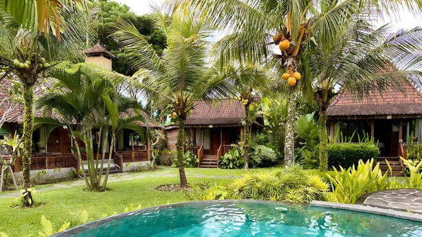Piscina rodeada por vegetação exuberante e edifícios de estilo tradicional com telhados de palha.