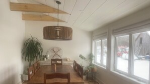 A spacious dining area with a large wooden table, multiple chairs, a hanging light fixture, and a view of a snowy outdoor area through large windows. - Beautifully restored Farmhouse on 64 acres+++ (Kimberley)