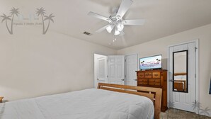 Un dormitorio con una cama, ventilador de techo, cómoda de madera y televisor sobre un mueble.