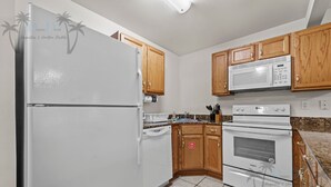 Una cocina con electrodomésticos blancos, armarios de madera, encimera de granito y suelo de baldosas.