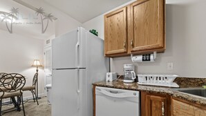Cocina compacta con refrigerador blanco, cafetera y lavavajillas.