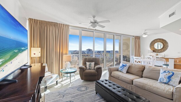 Een ruime woonkamer met een grote flatscreen televisie, een comfortabele bank, een relax fauteuil en een balkon met uitzicht op de oceaan.