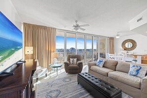 A spacious living room with a large flat-screen TV, a comfortable sofa, a recliner, and a balcony with a view of the ocean. - Sanibel 404 by Liquid Life (Gulf Shores)