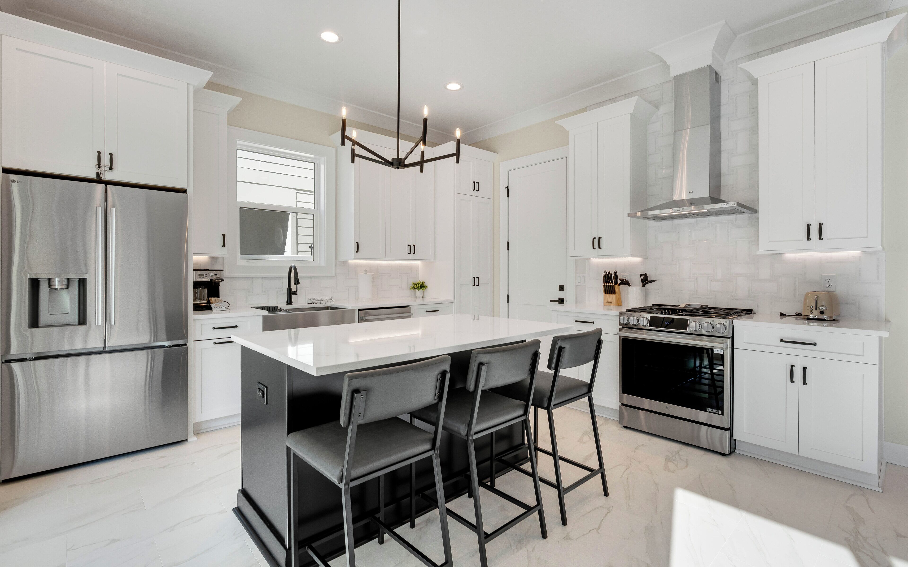 A modern kitchen with white cabinetry, stainless steel appliances, a central island with bar stools, and a pendant light.