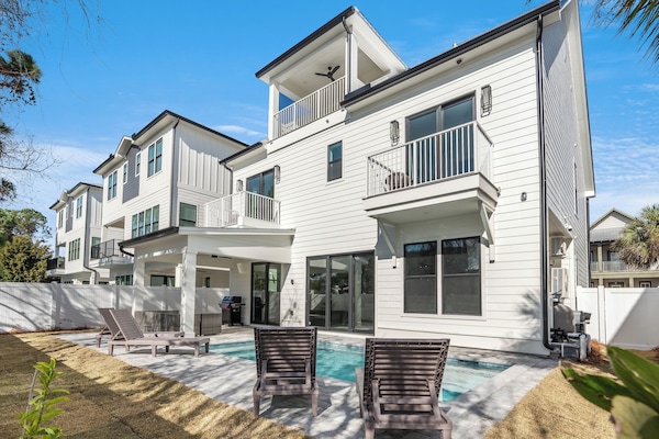 Modern multi-story vacation home with private pool, outdoor lounging area, and tropical landscaping in a peaceful neighborhood setting.