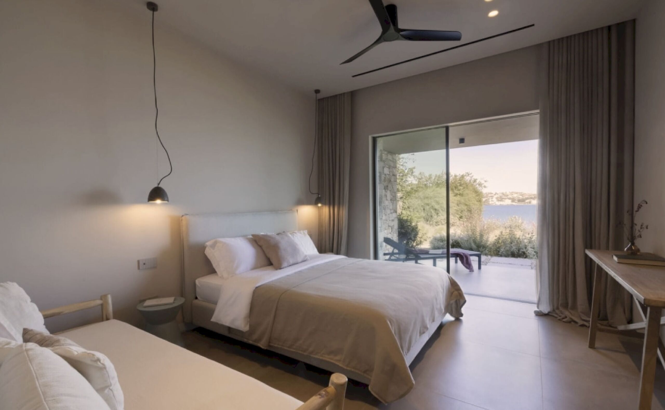 A modern bedroom with a large bed, a desk, and a view of the outdoors.