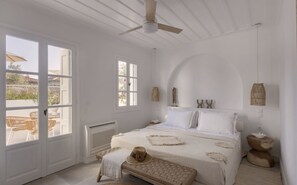 Ein Schlafzimmer mit Bett, Sitzbank, Deckenventilator und Ausblick ins Freie.