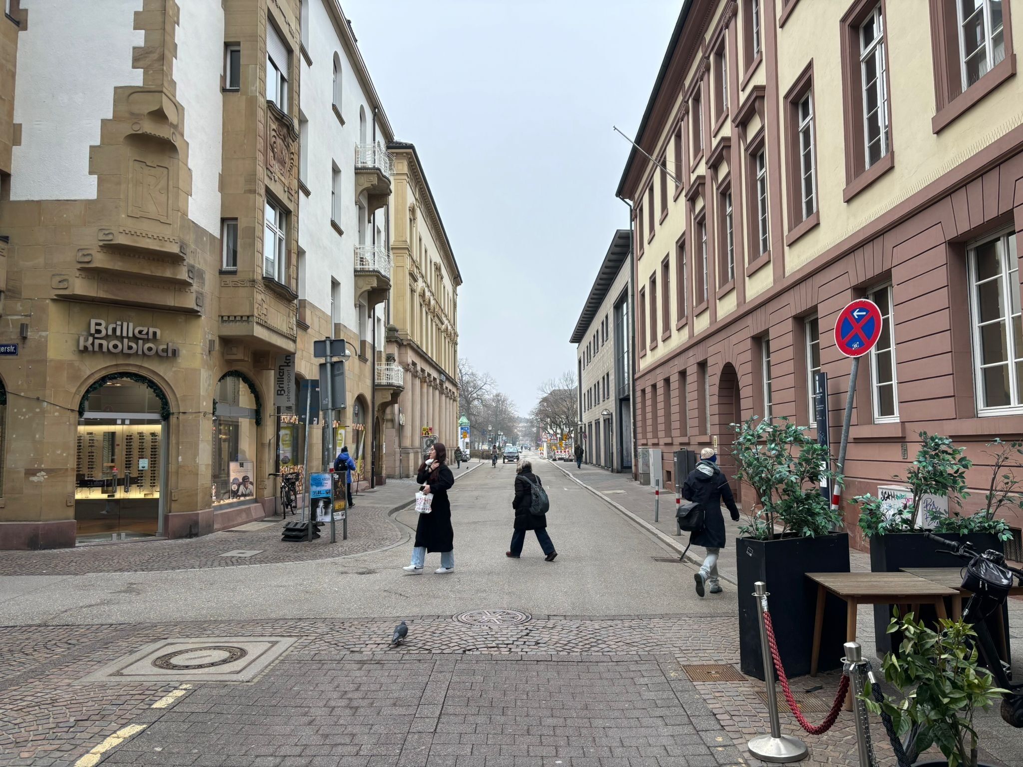 A street with buildings, a no parking sign, and pedestrians.
