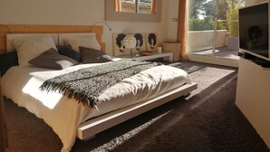 Een slaapkamer met een bed, een televisie, een raam met gordijnen en kunst aan de muur.