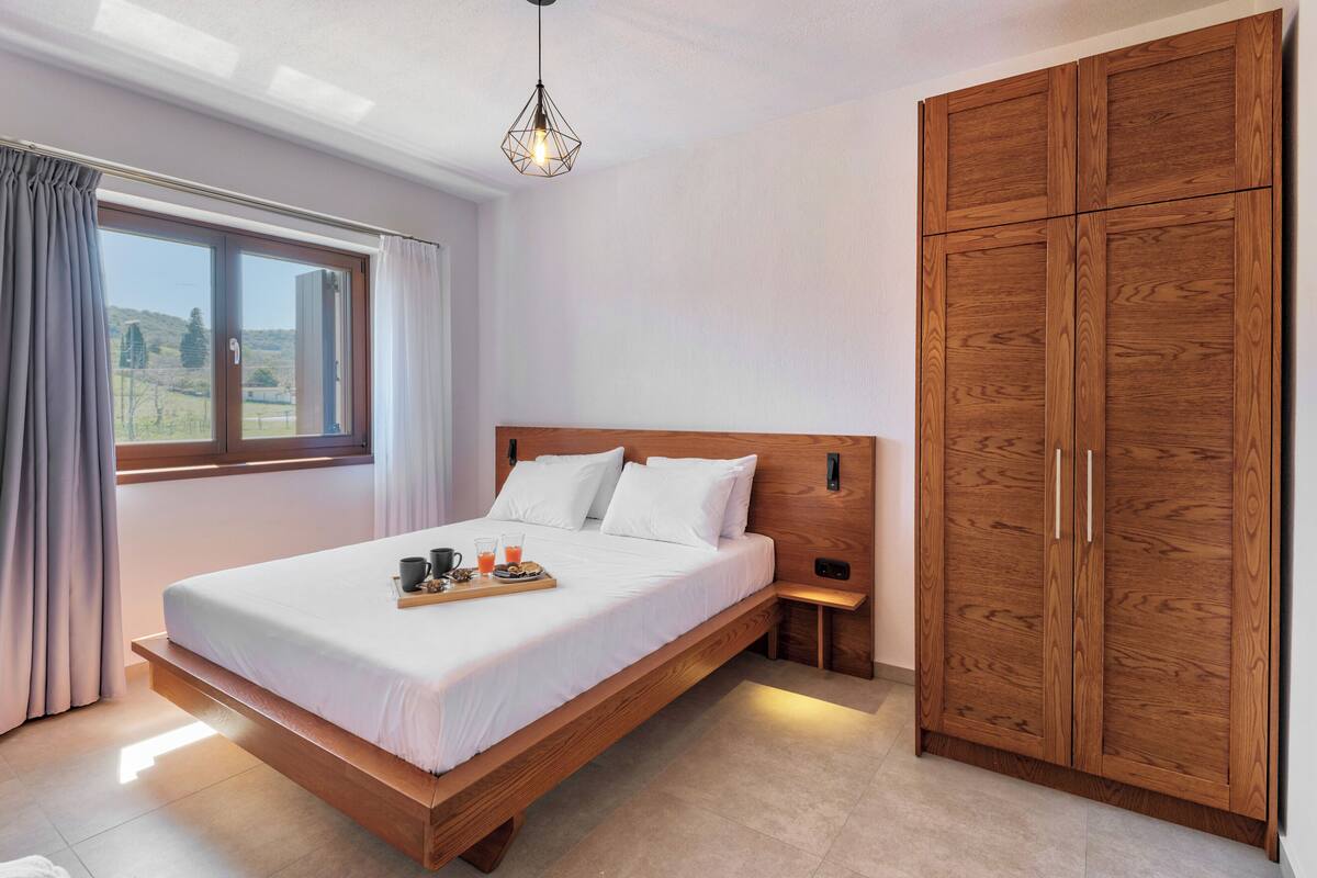 Ein Schlafzimmer mit einem Holzbett, einem Nachttisch, einem Kleiderschrank und einem Fenster mit Vorhängen.
