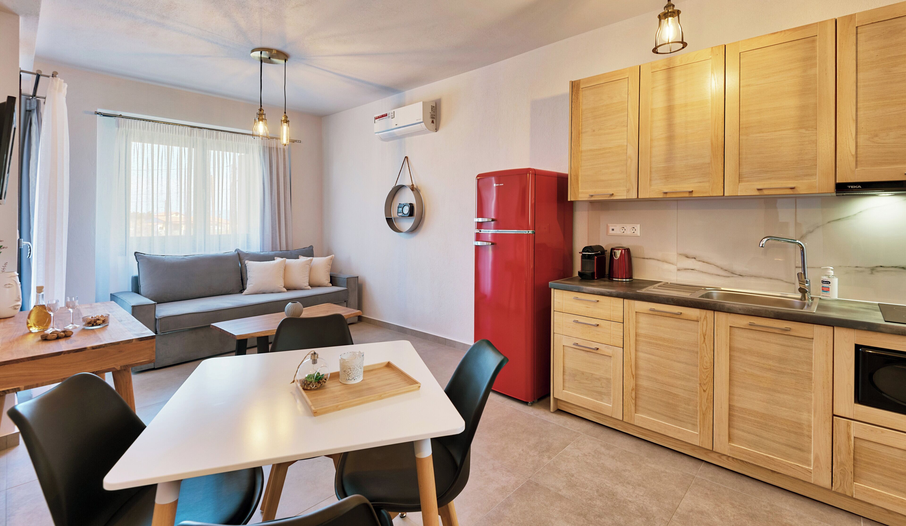 A compact living space with a dining area, a kitchen with wooden cabinets, a red refrigerator, and a ceiling light fixture.