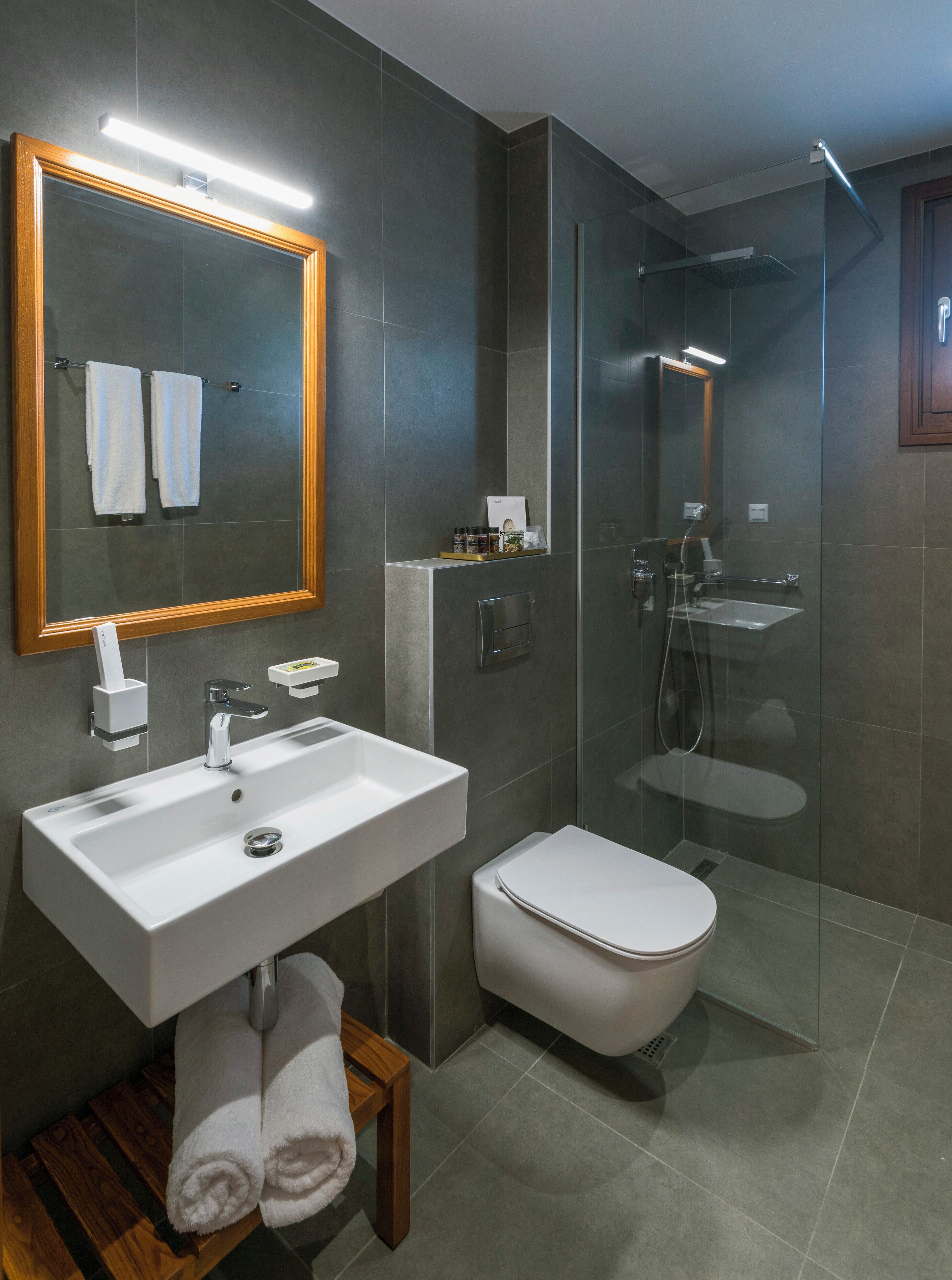 A modern bathroom with a large mirror, white sink, toilet, and glass shower enclosure.